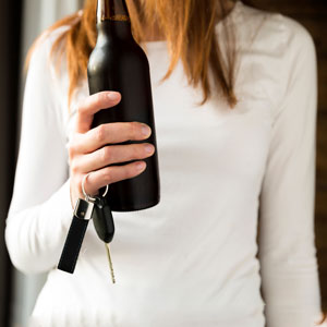 A woman holding a bottle of liquor and a car key in hand, potentially about to drive under the influence (DUI).